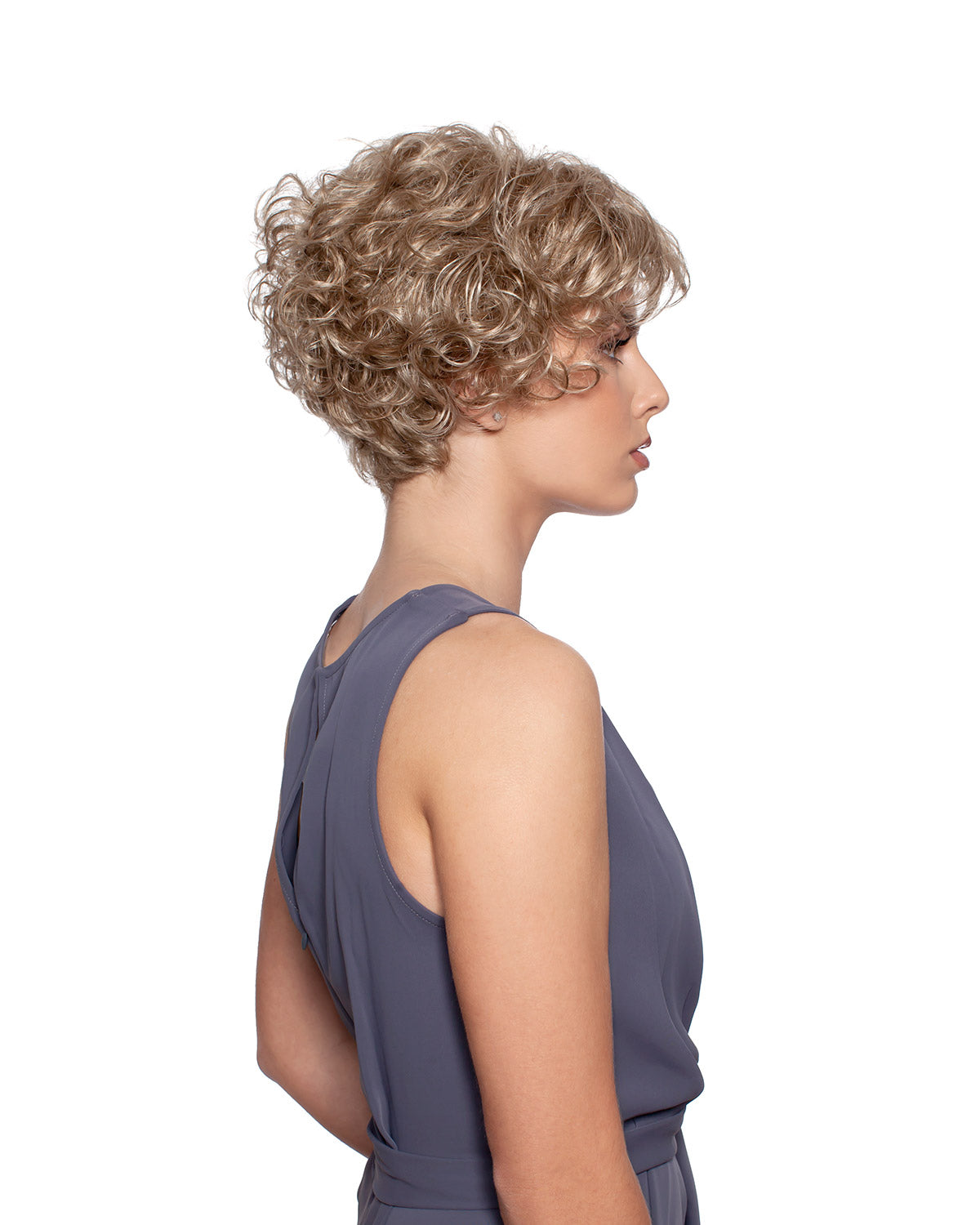 Woman wearing Annie synthetic curly wig by WigPro and a grey sleevelss top against a white background - right side view