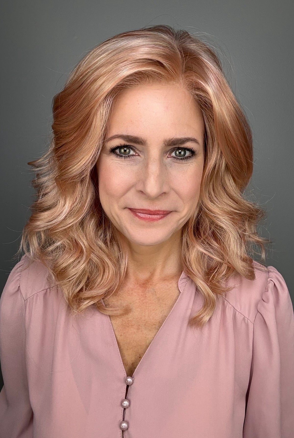 A woman with shoulder-length wavy pink wig (Avalon by Estetica in color Smoky Rose).