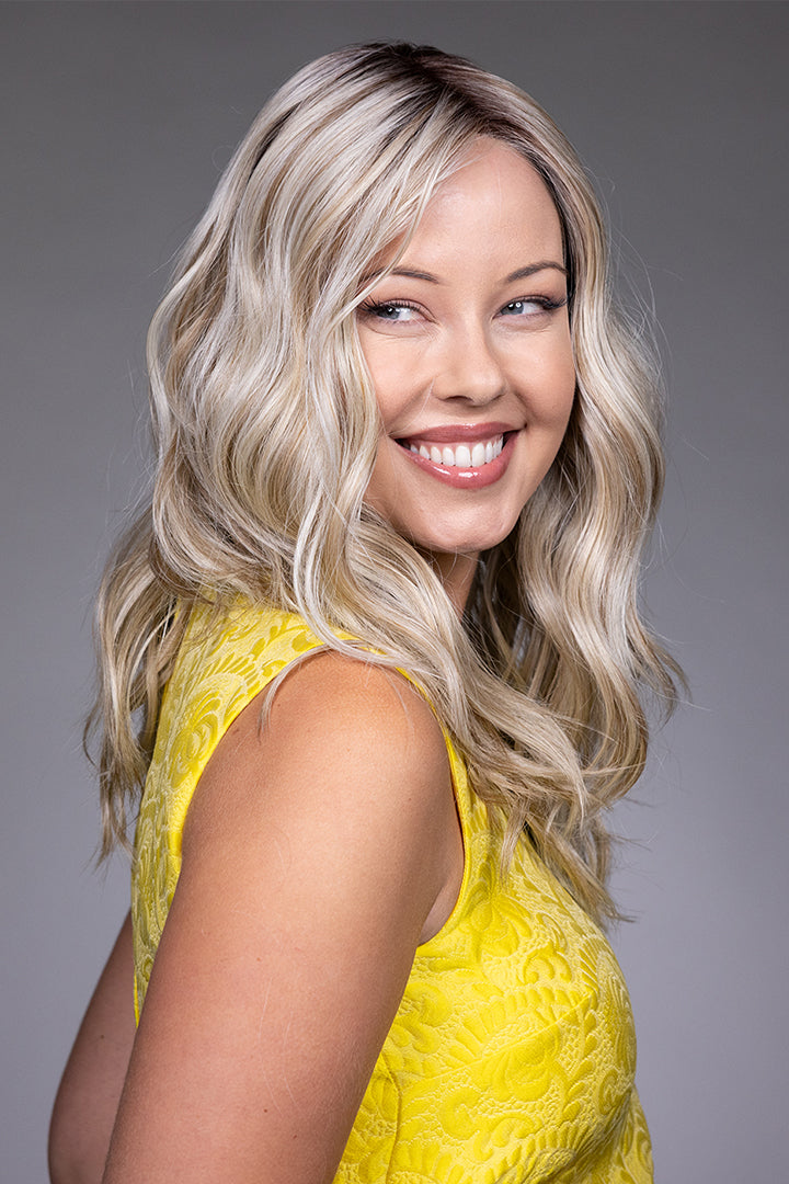 Bella by Belle Tress long wavy blonde synthetic wig with lace front and monofilament top on a smiling woman.