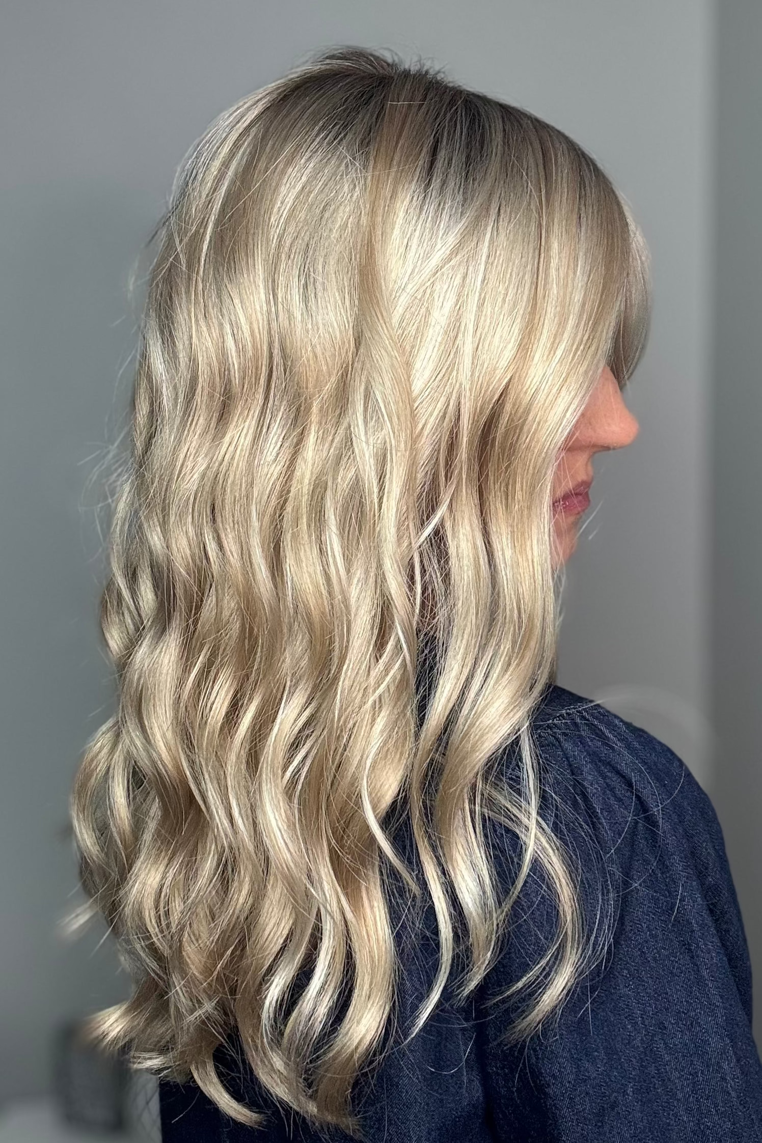 Woman with long rooted blonde wavy wig. (Maya Hand-Tied by Envy in Silky Beige).
