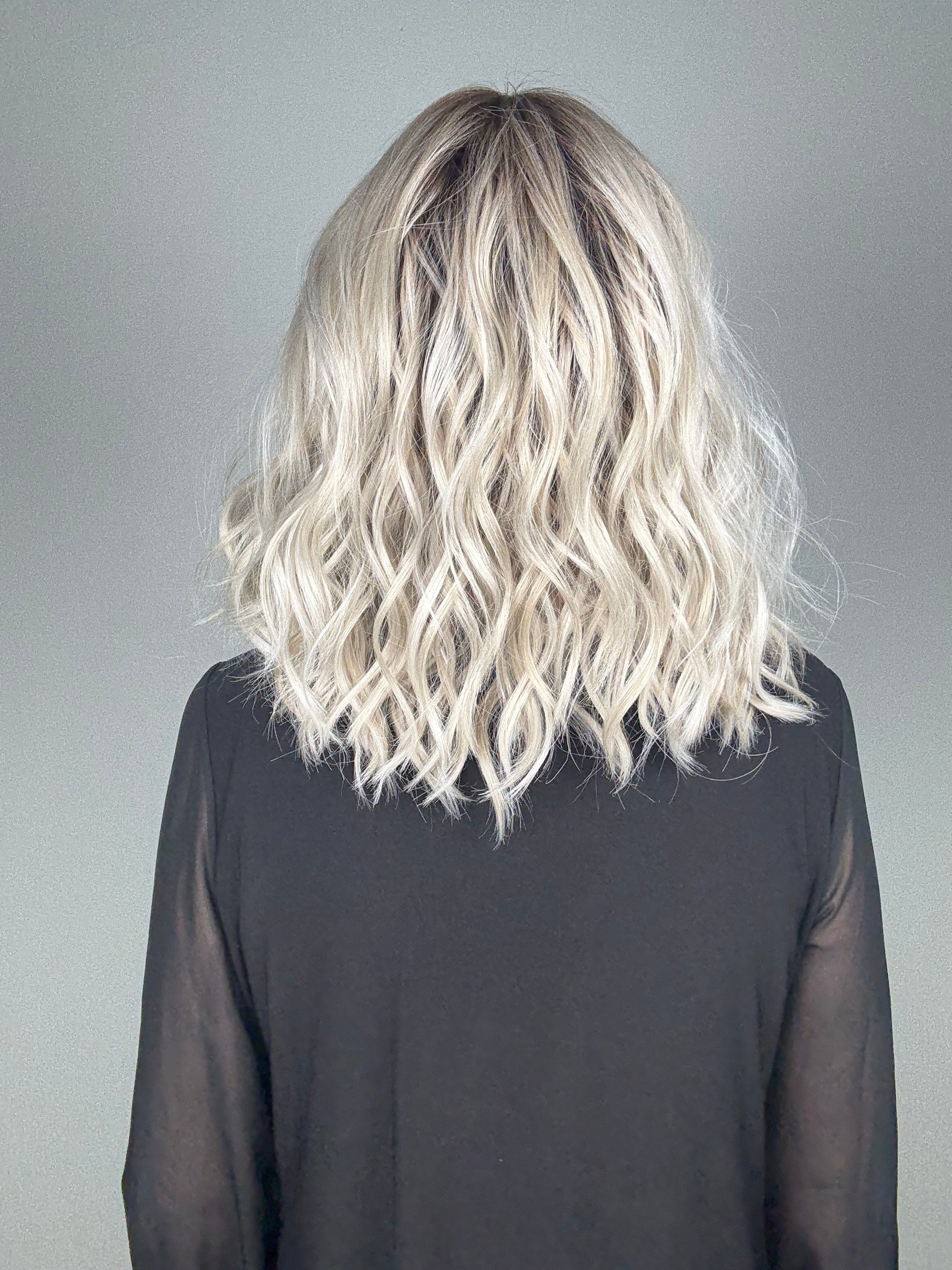 Woman wearing wavy rooted blonde wig with bangs (Frankie by Estetica in Silver Sun RT8) back