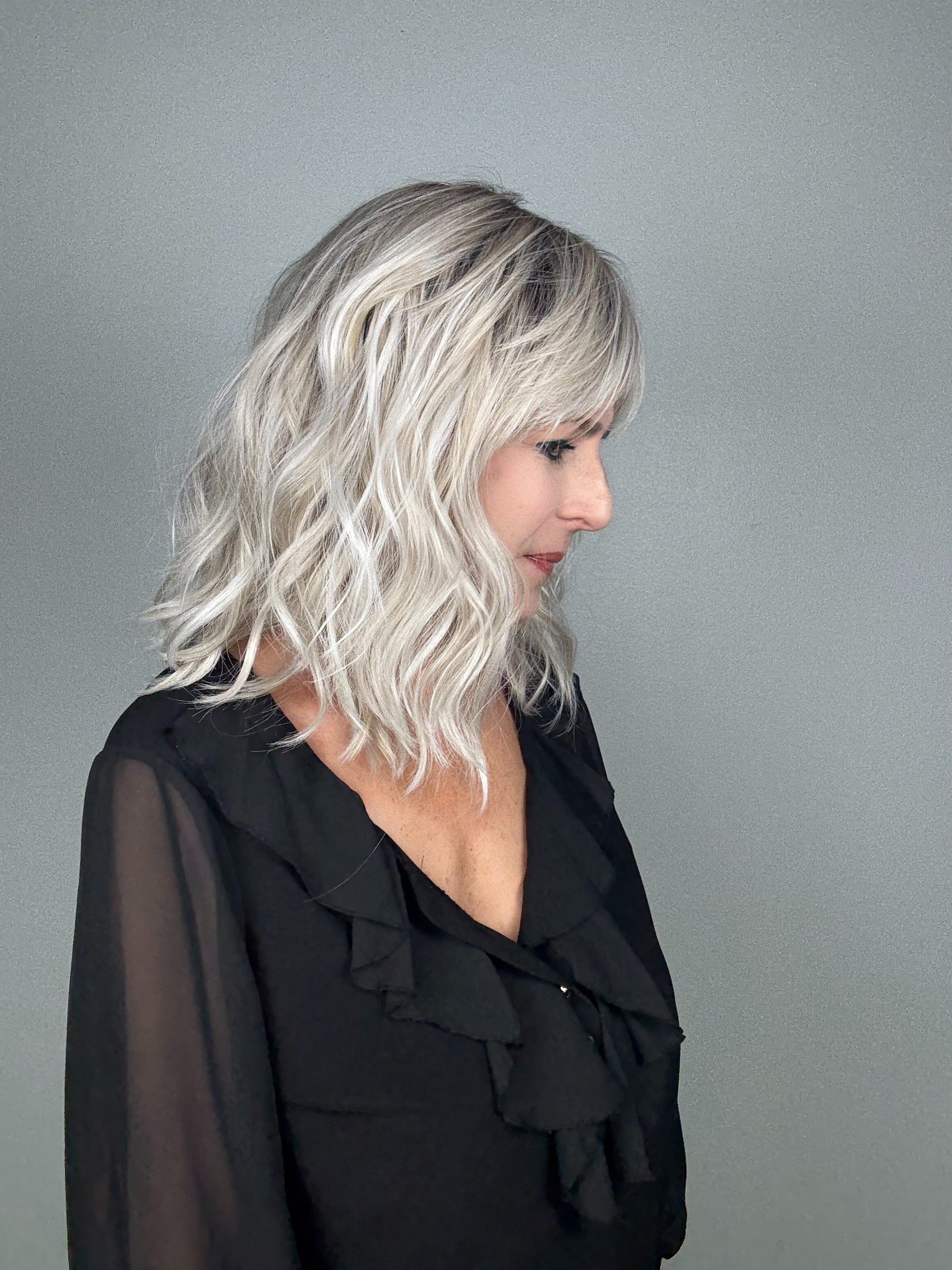 Woman wearing wavy rooted blonde wig with bangs (Frankie by Estetica in Silver Sun RT8) side