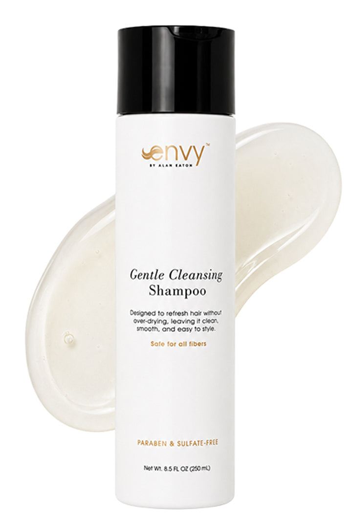 A bottle of Envy by Hair Gentle Cleansing Shampoo with a black cap and white bottle, shown in front of a translucent smear of the shampoo on a white background.