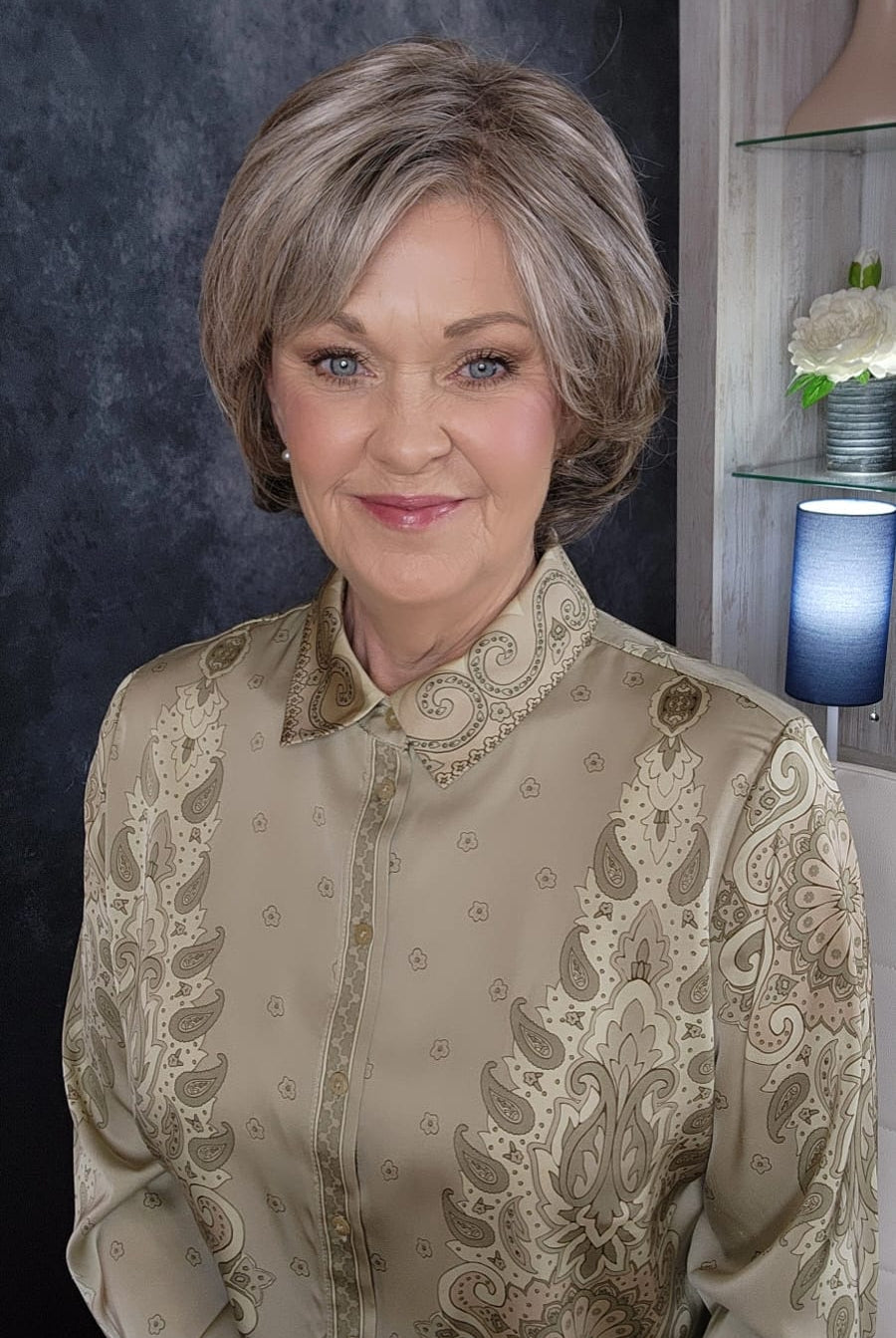Woman wearing an ashy gray-brown bob wig with bangs (Gianna by Henry Margu in color 37)