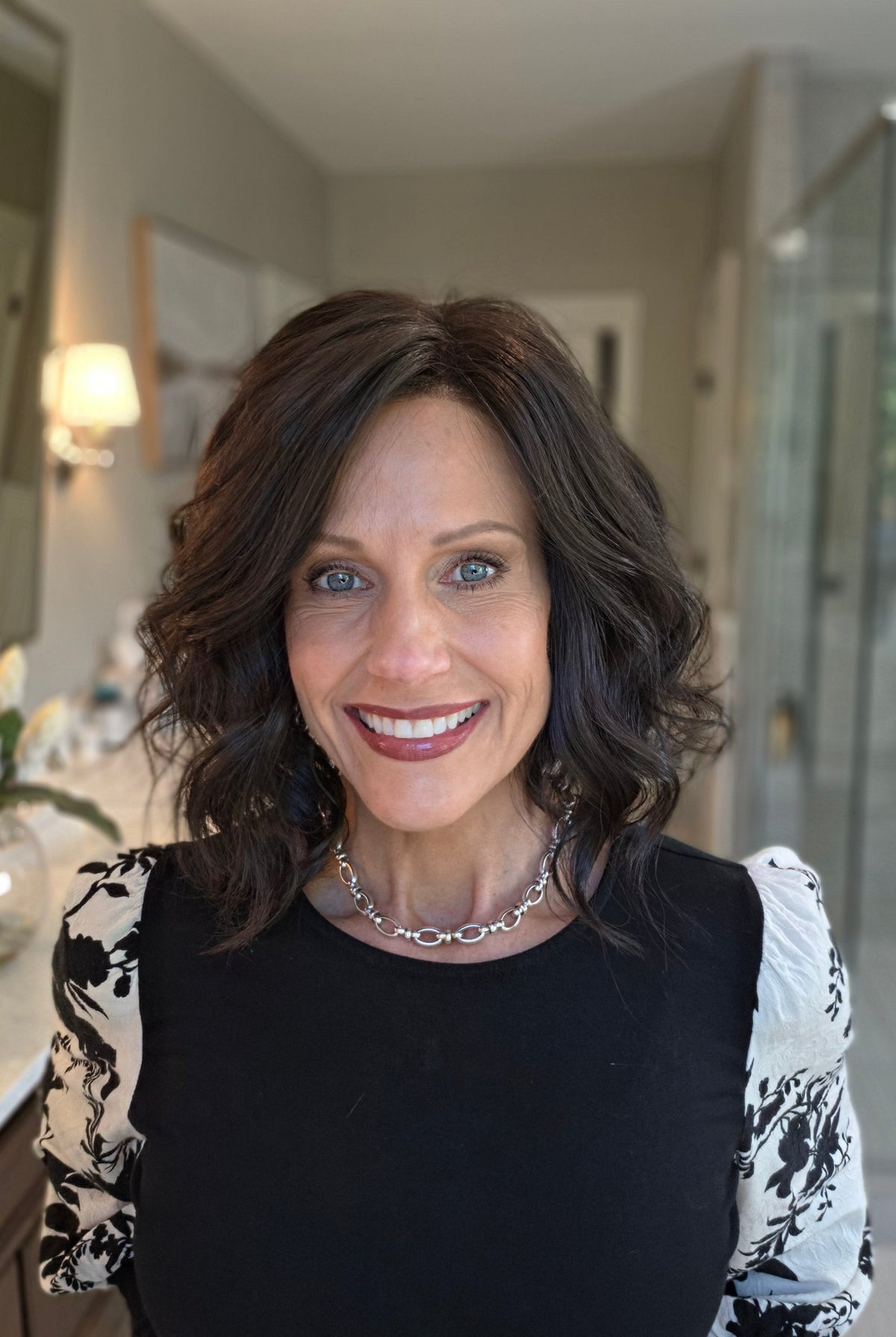 A smiling woman with shoulder-length dark brown wavy wig (Lacy Lite by Jon Renau in 4).