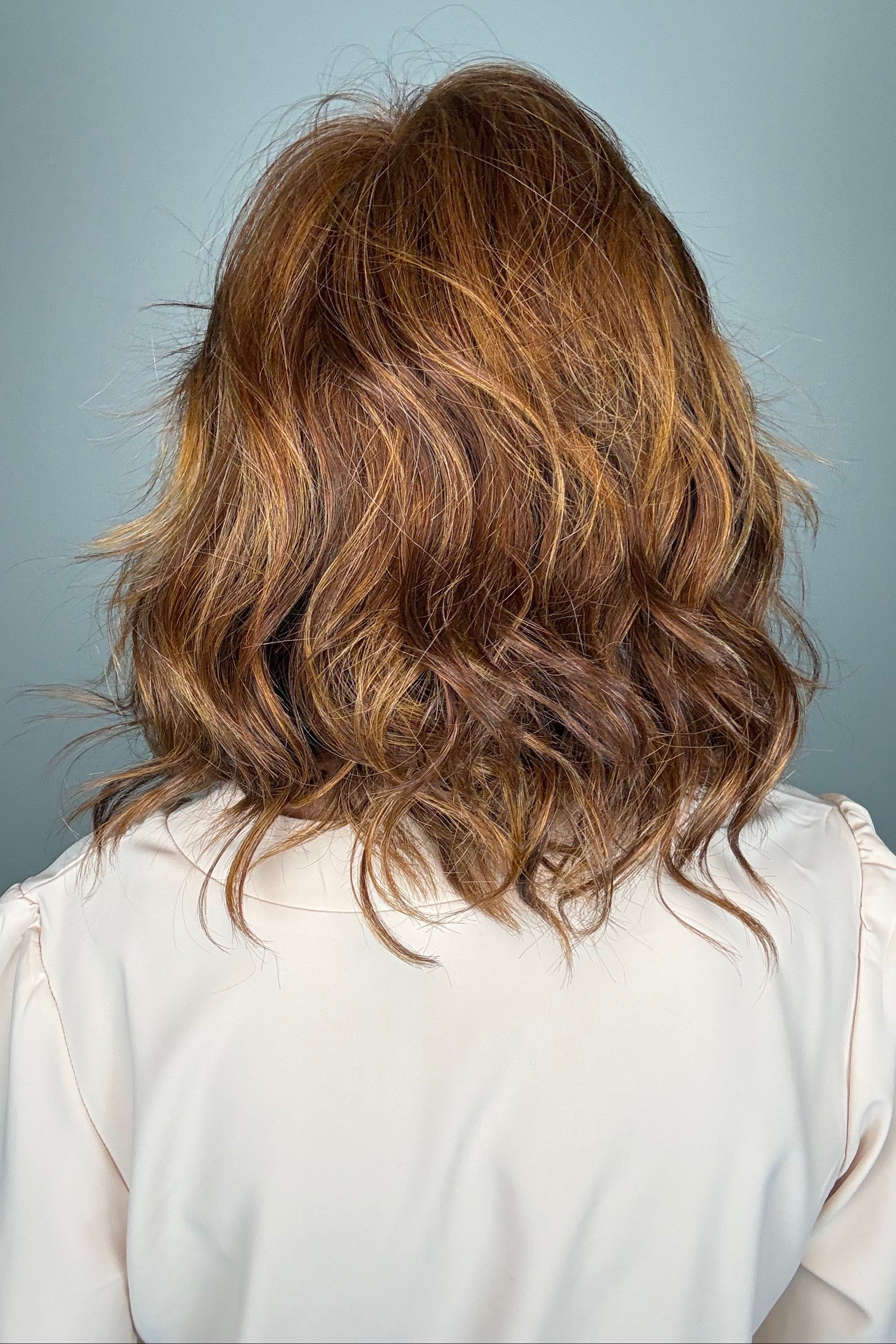 A woman with a shoulder-length wavy red wig with bangs (Lively by Gabor in Medium Red).