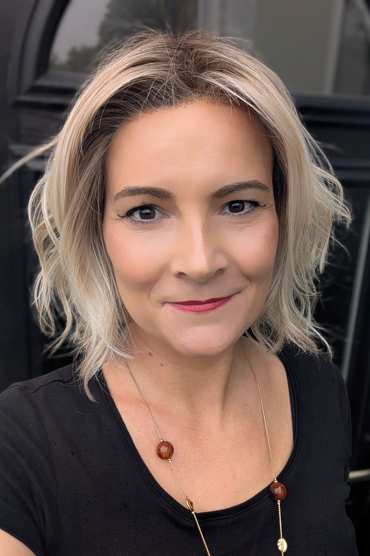 A woman with short blonde wavy bob wig (Naples by Belle Tress in color Crushed Almond Blonde R).