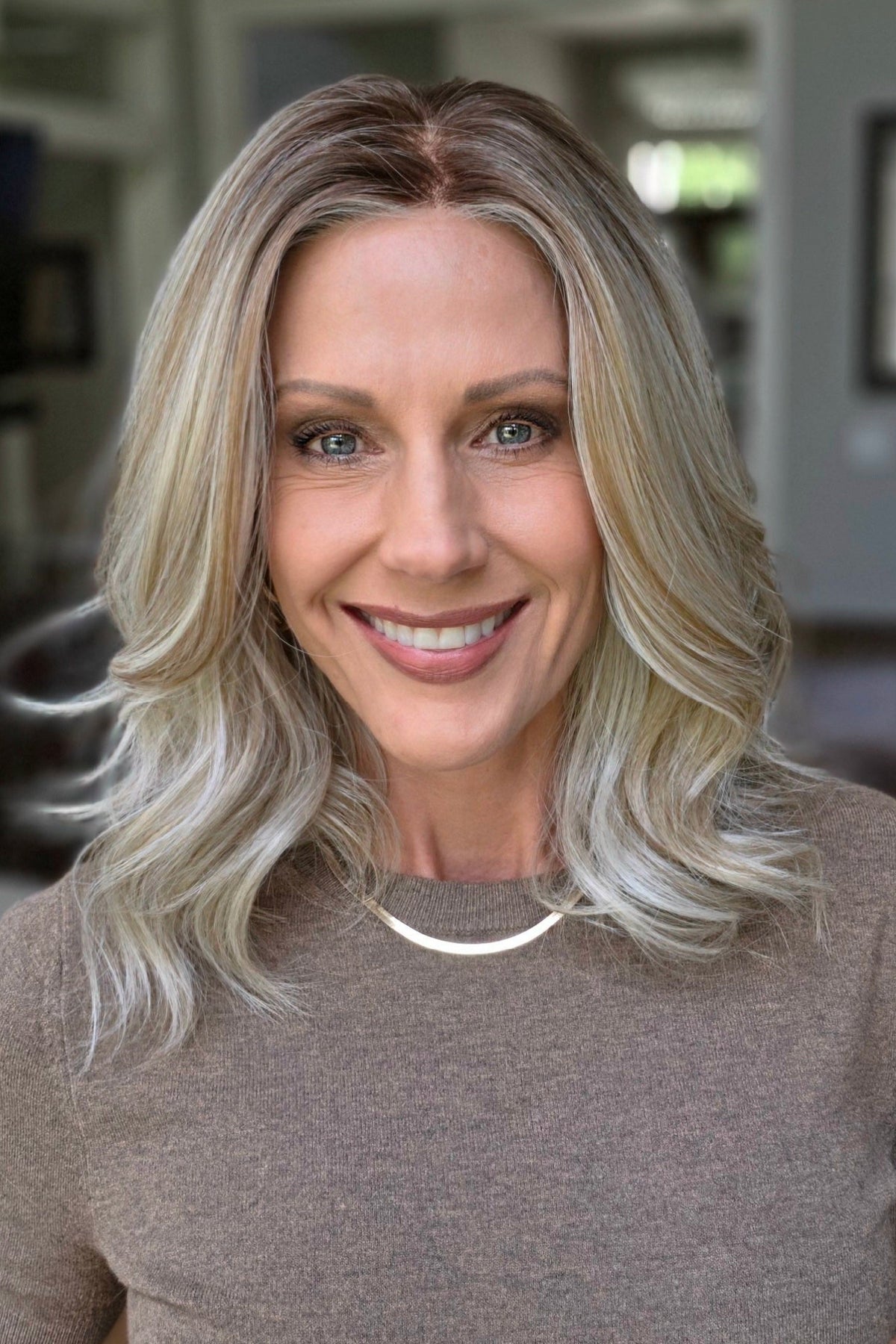 A smiling woman with shoulder-length wavy blonde wig (Keeley by PUSH Hair in color Champagne Blonde R).