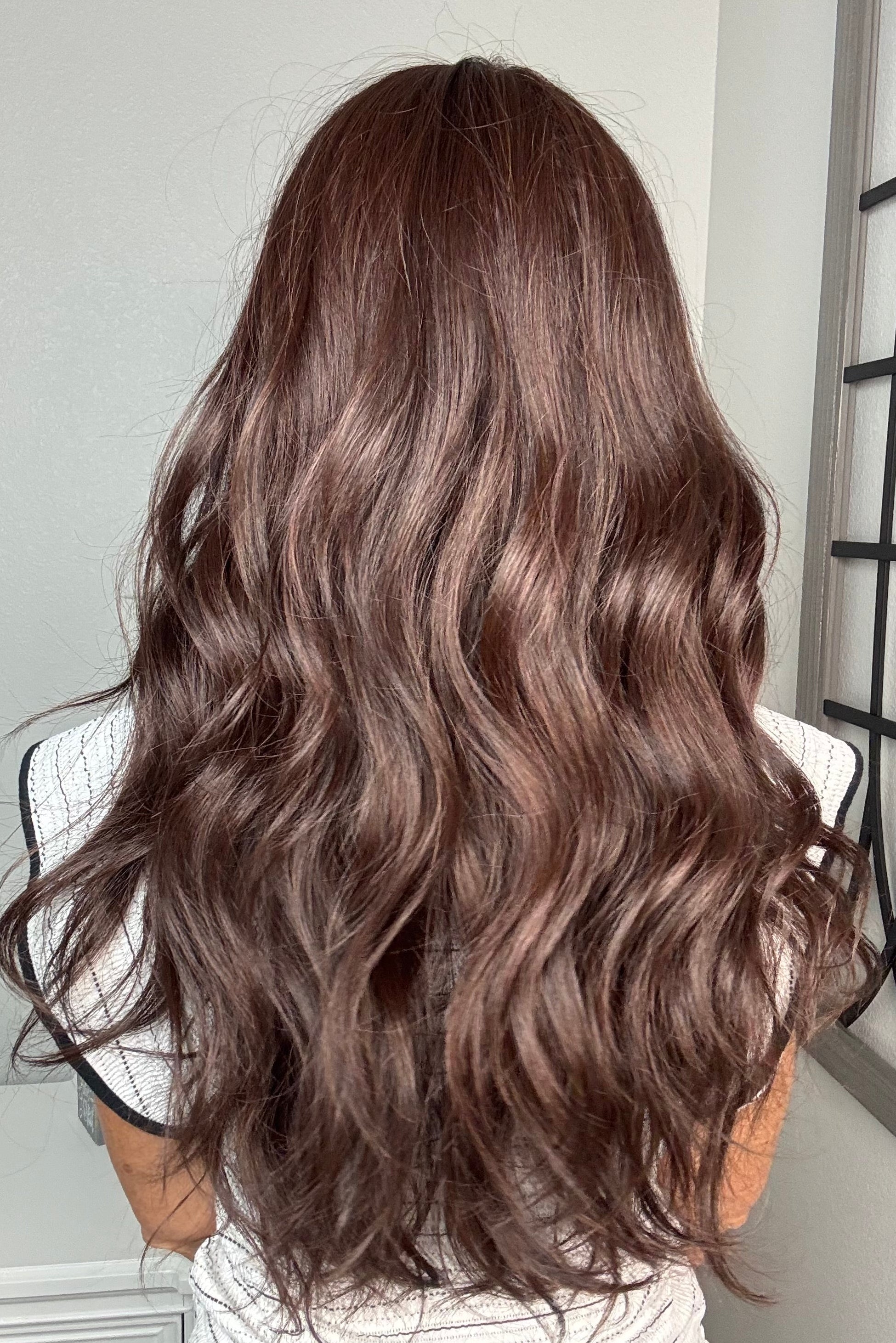 A woman with long, wavy dark brown hair wearing a black and white striped sleeveless top with black trim (Bradley by PUSH Hair in color Dark Chocolate Chestnut).
