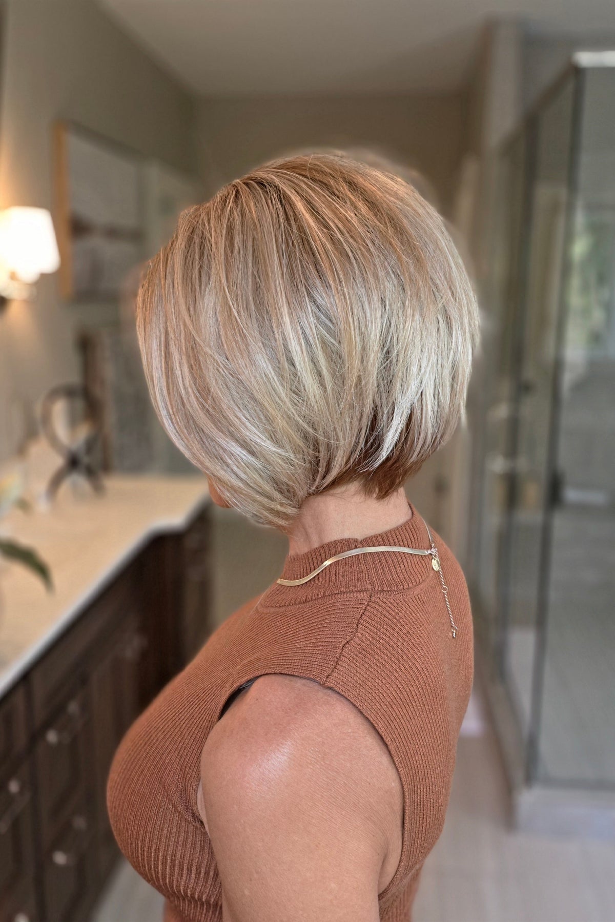 A woman with a short blonde bob hairstyle wearing a ribbed sleeveless rust-brown top (Maggie by Rene of Paris in Winter Oak Latte R).