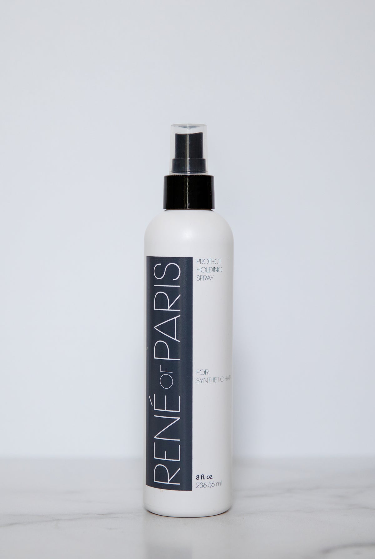 A white bottle of René de Paris Moist Locking Spray with a black spray nozzle, standing on a light marble surface against a plain light gray background.