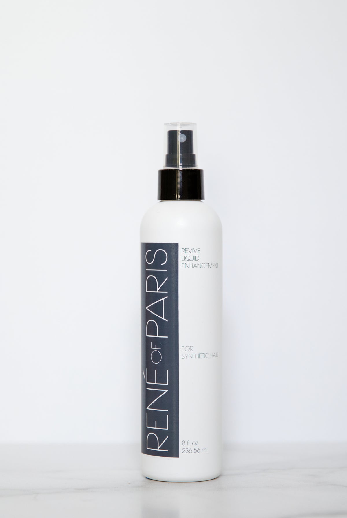 A white bottle of Rene-For-Paris Blue Blue Enhancer spray with a black pump and clear cap, standing on a light marble surface against a white background.