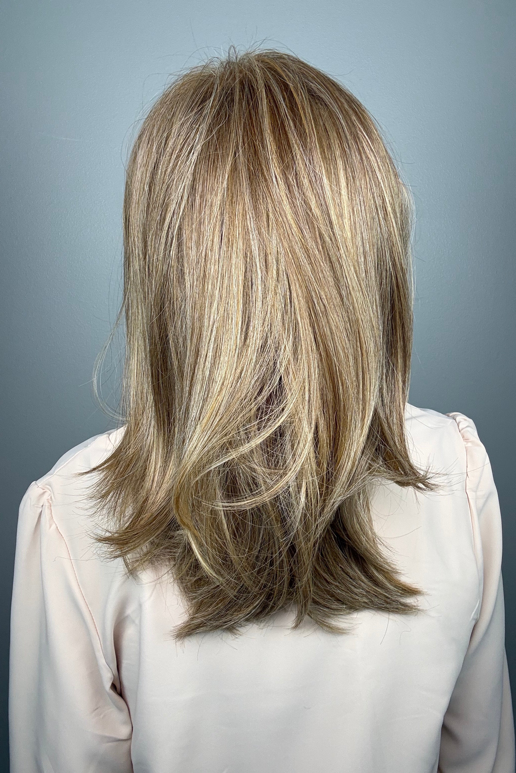 Woman wearing layered golden blonde wig with bangs (Whisper by Henry Margu in 12/26H)