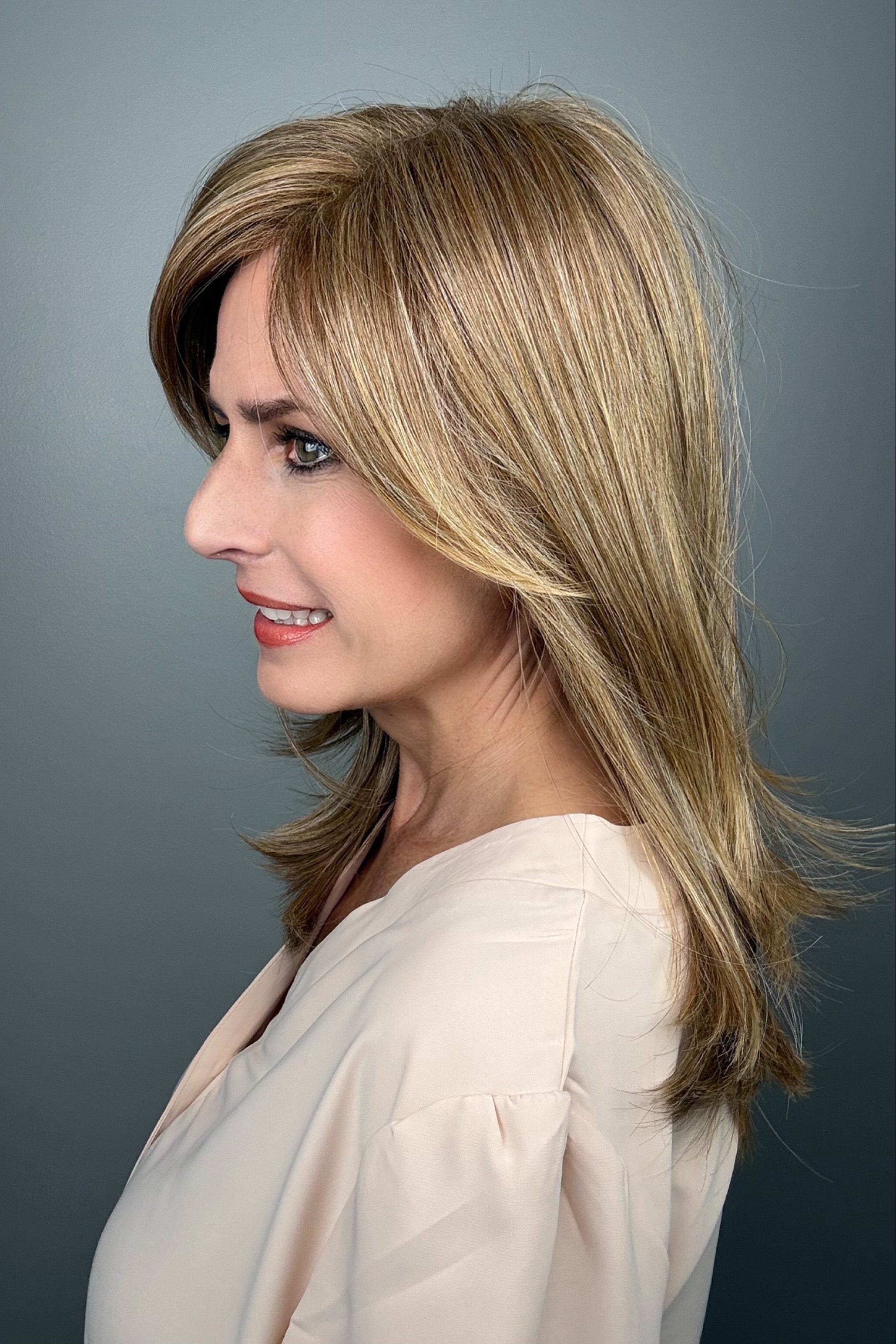 Woman wearing layered golden blonde wig with bangs (Whisper by Henry Margu in 12/26H)