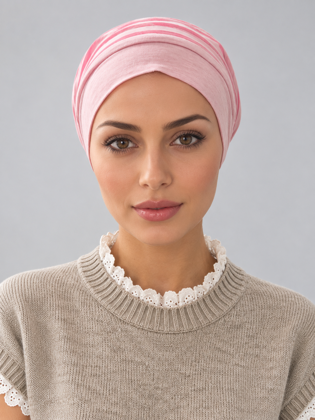 A woman wearing a rose melange turban-style head covering and a beige knit sweater with a white lace collar, photographed against a plain light gray studio background.
