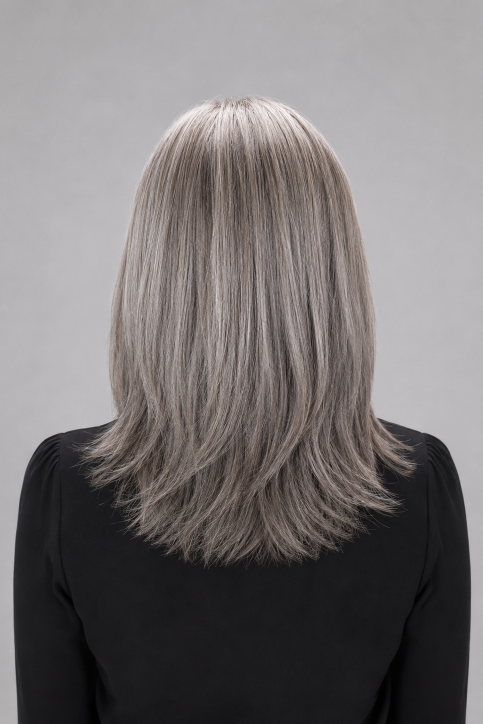 Woman wearing a Bespoke human hair wig by PUSH hair in color Sage, wearing a black blouse against a light grey background - back view