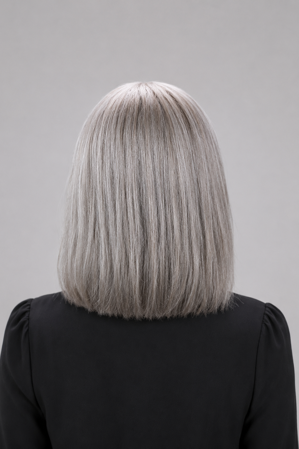 Woman wearing Bespoke human hair wig by PUSH - 16" inverted bob wig in color sage with a black blouse against a light grey background - back view