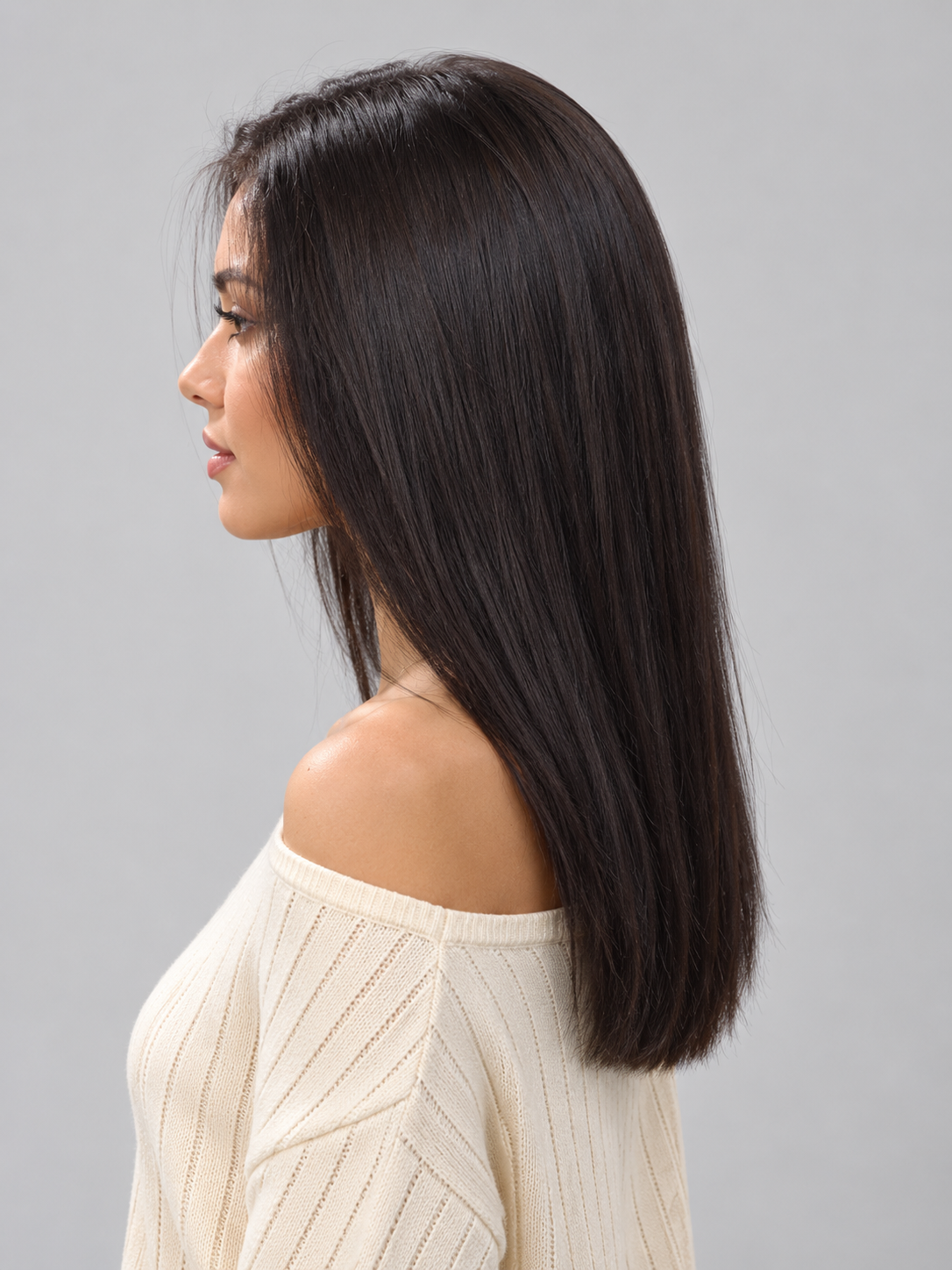 Woman wearing Gisele human hair wig by PUSH in color Noir and a cream off the shoulder knit top against a light grey background - left side view.