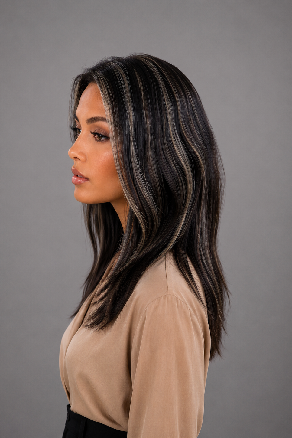 Woman wearing Gisele Human Hair Wig by PUSH in color Étoile Nocturne, a deep and rich off black base with chunky blonde highlights throughout and a tan blouse against a light grey background. Right side view.