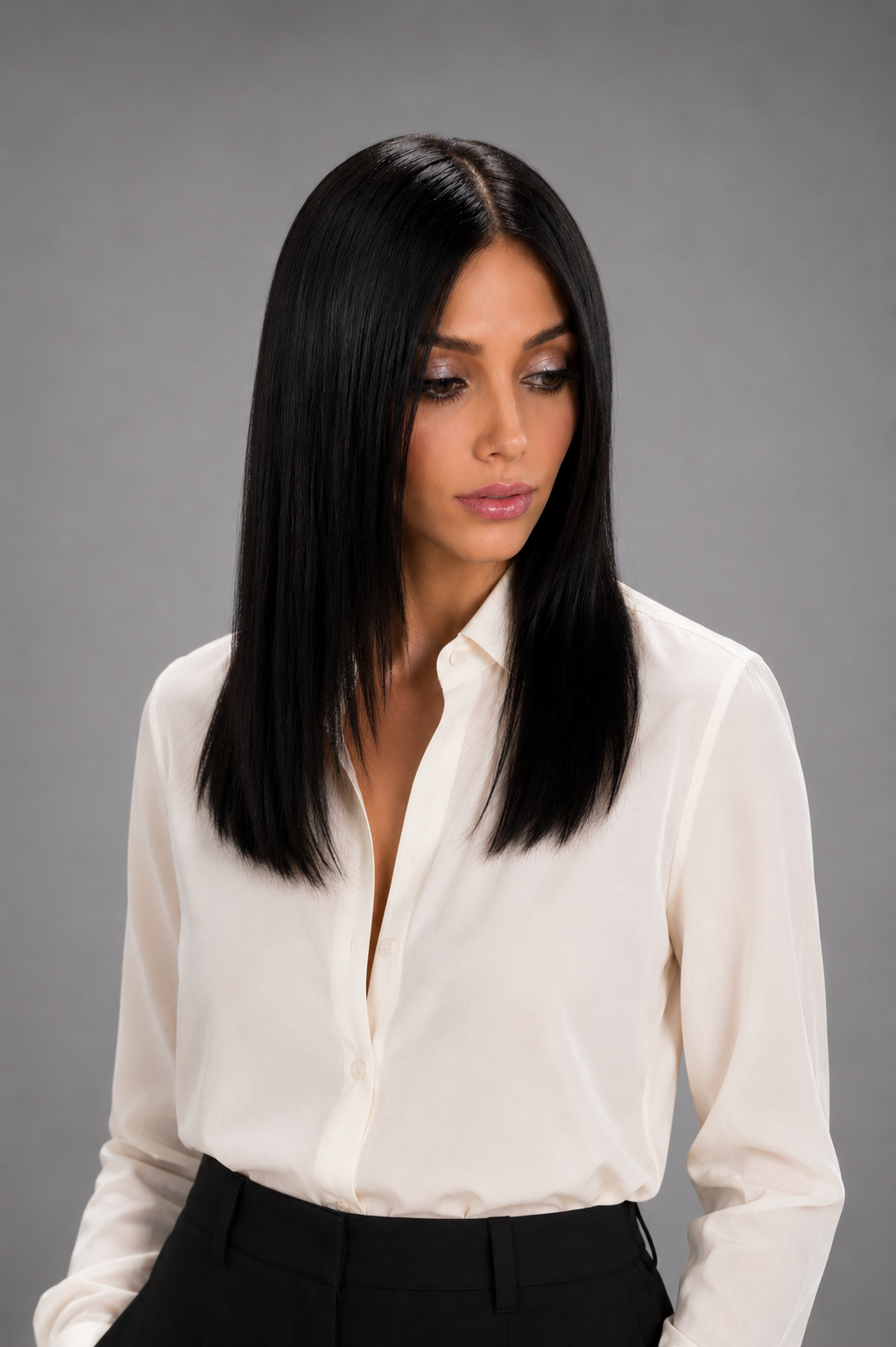 Woman wearing Jacey human hair wig by PUSH in color Noir with cream button down blouse and black pants with a light grey background. Front view.
