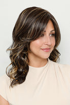 Sage by Henry Margu medium-length wavy wig with face-framing layers and sweeping side fringe in a highlighted brown shade.