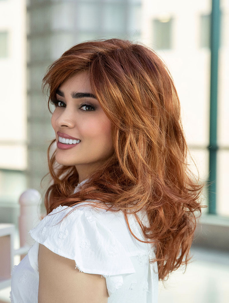 Woman wearing Alana synthetic wig by Envy in color Lighter Red wearing a white blouse in an indoor setting. Left side