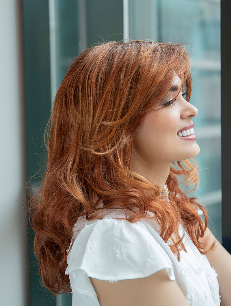 Woman wearing Alana synthetic wig by Envy in color Lighter Red wearing a white blouse in an indoor setting. Right side.