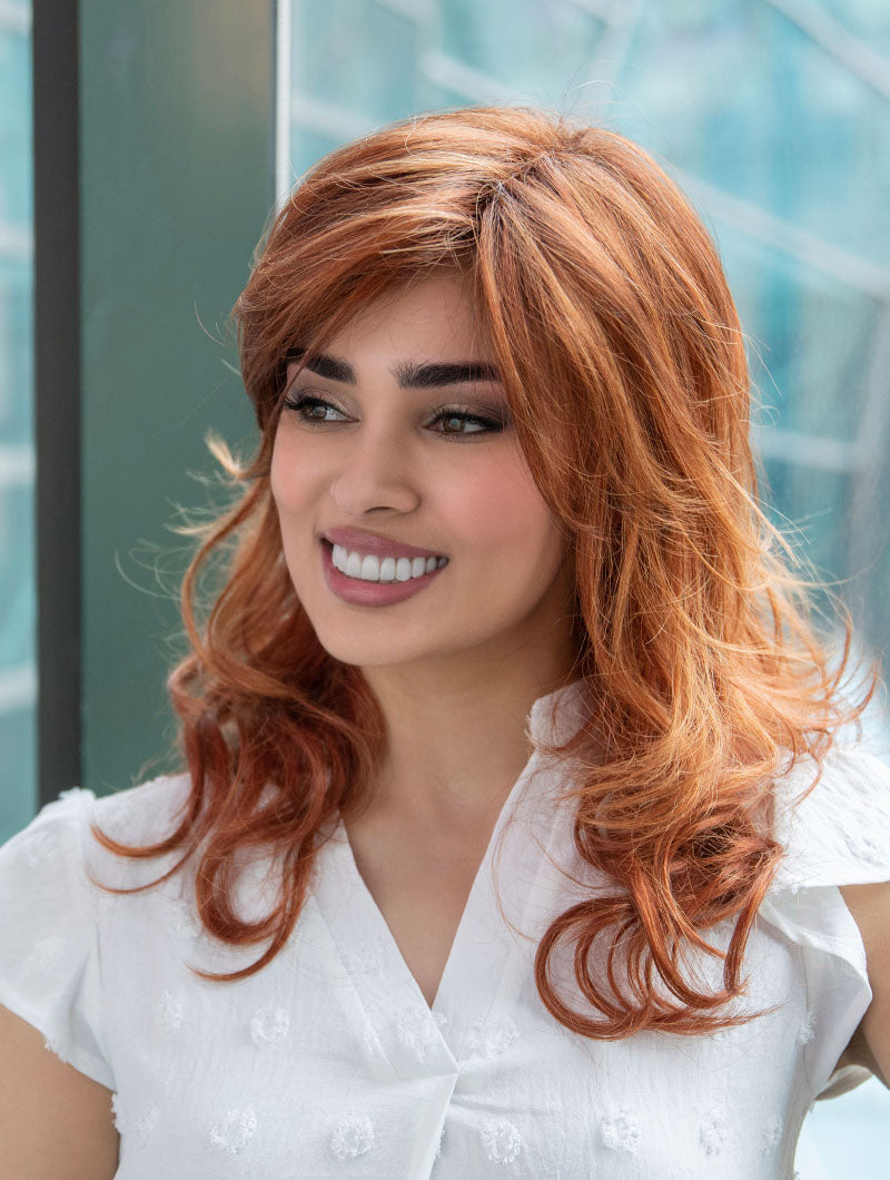 Woman wearing Alana synthetic wig by Envy in color Lighter Red wearing a white blouse in an outdoor setting.