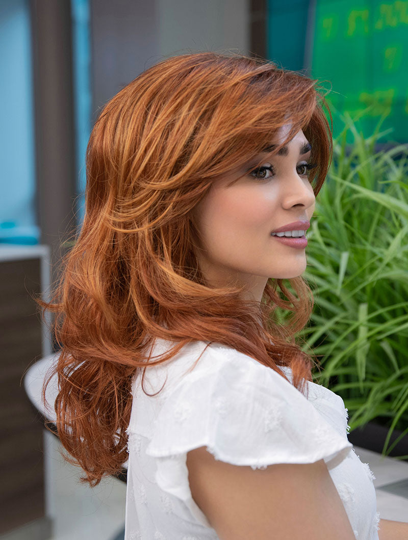 Woman wearing Alana synthetic wig by Envy in color Lighter Red wearing a white blouse in an outdoor setting.