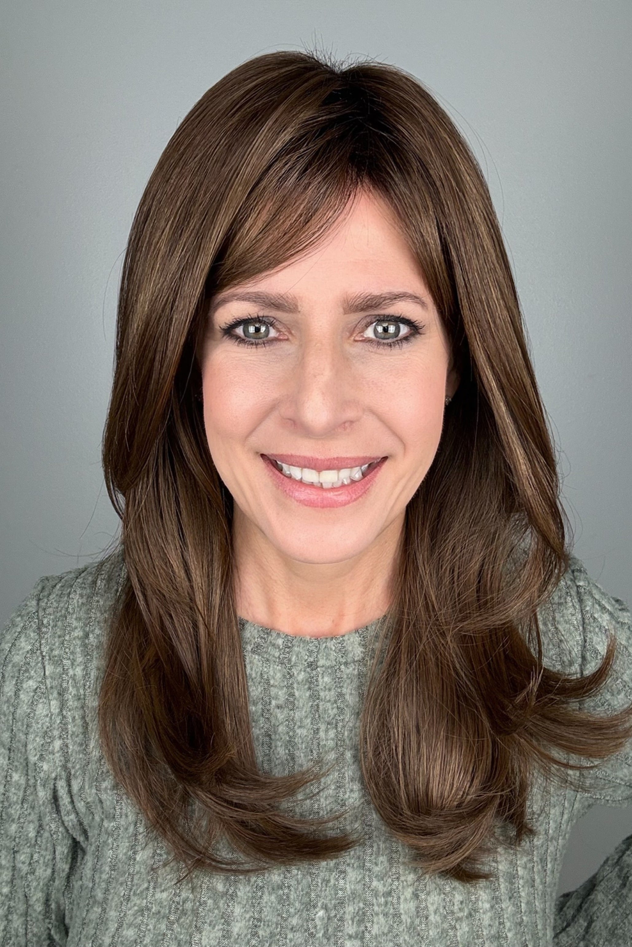 A woman with shoulder-length brown hair and bangs, wearing a textured light gray knit sweater (All Grown Up by Toni Brattin in color Light Brown).