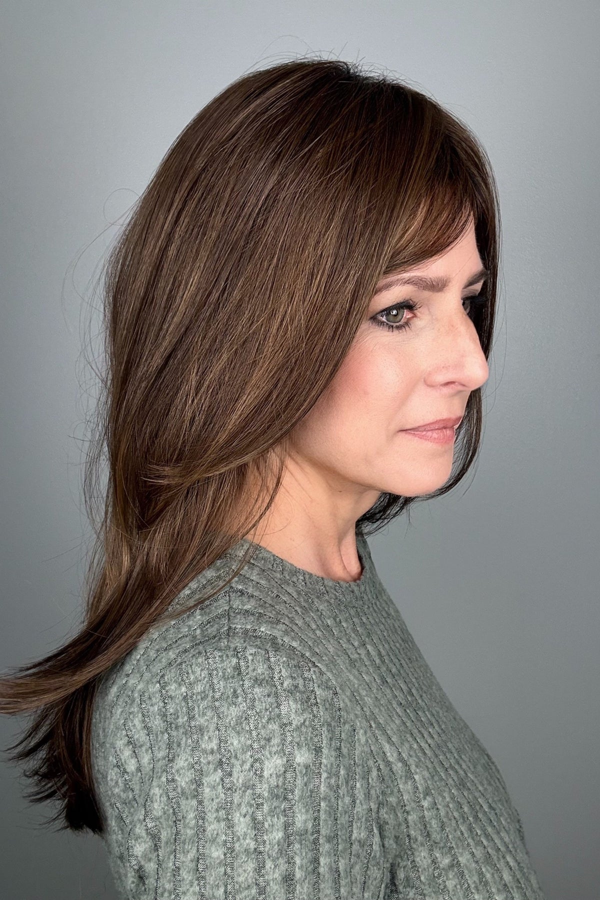A woman with shoulder-length brown hair and bangs, wearing a textured light gray knit sweater (All Grown Up by Toni Brattin in color Light Brown).