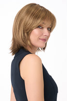 Woman wearing Amber by Envy synthetic lace front wig with shoulder-length layered blonde hair and bangs.