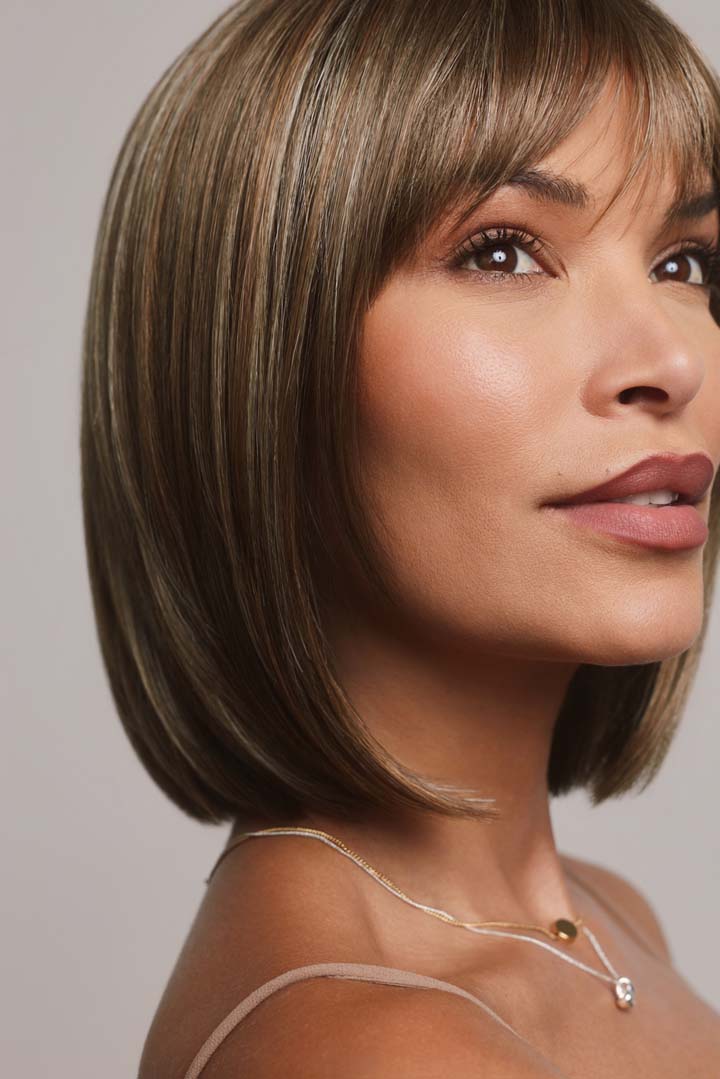 Ami by Noriko medium-length synthetic bob wig with face-framing layers and bangs in a highlighted brown shade.