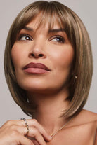 Ami by Noriko synthetic medium-length bob wig with face-framing layers and bangs in a natural highlighted brown shade.
