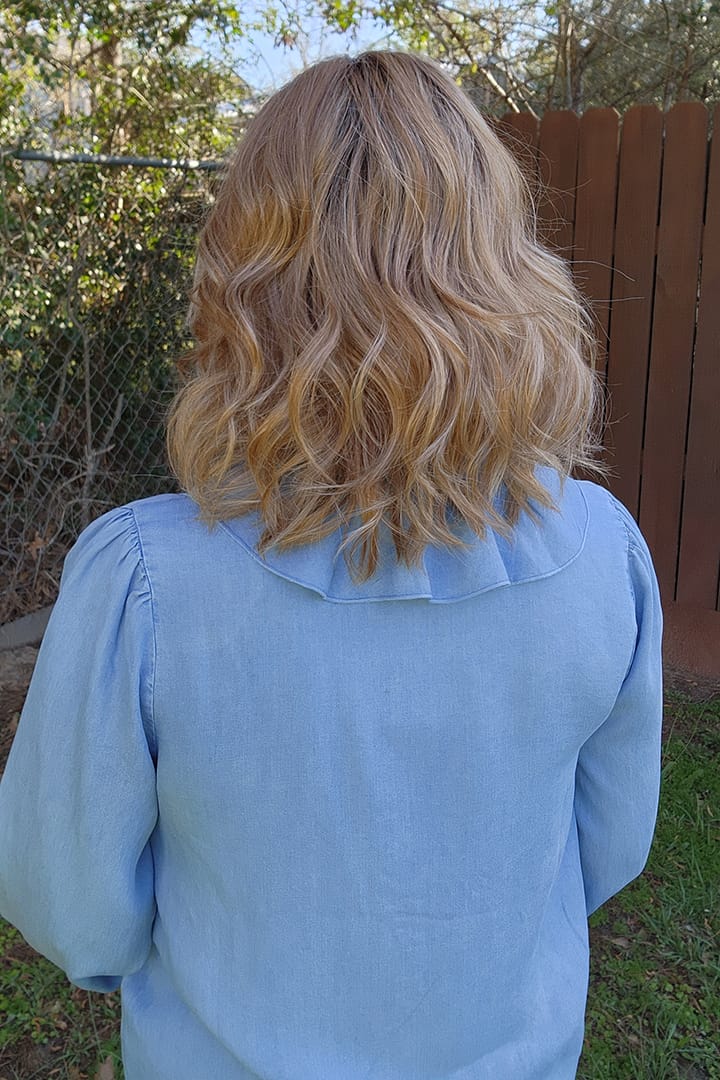 Woman wearing curled shoulder-length wig (Rohan by Amore in color Cinnamon Frost R) back