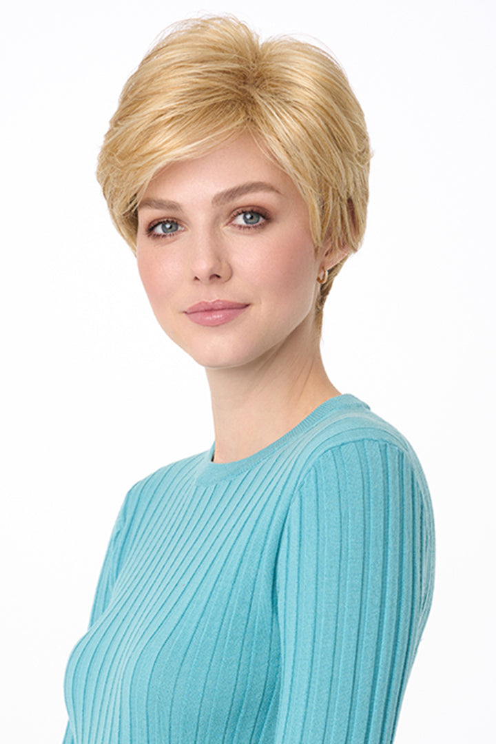 Blonde synthetic pixie wig with long bangs on a woman wearing a blue ribbed top.