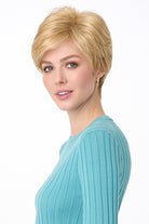 Blonde synthetic pixie wig with long bangs on a woman in a blue top.