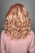 A woman with shoulder-length wavy pink wig (Avalon by Estetica in color Smoky Rose).