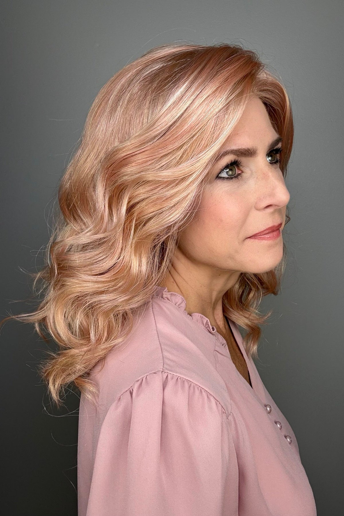 A woman with shoulder-length wavy pink wig (Avalon by Estetica in color Smoky Rose).