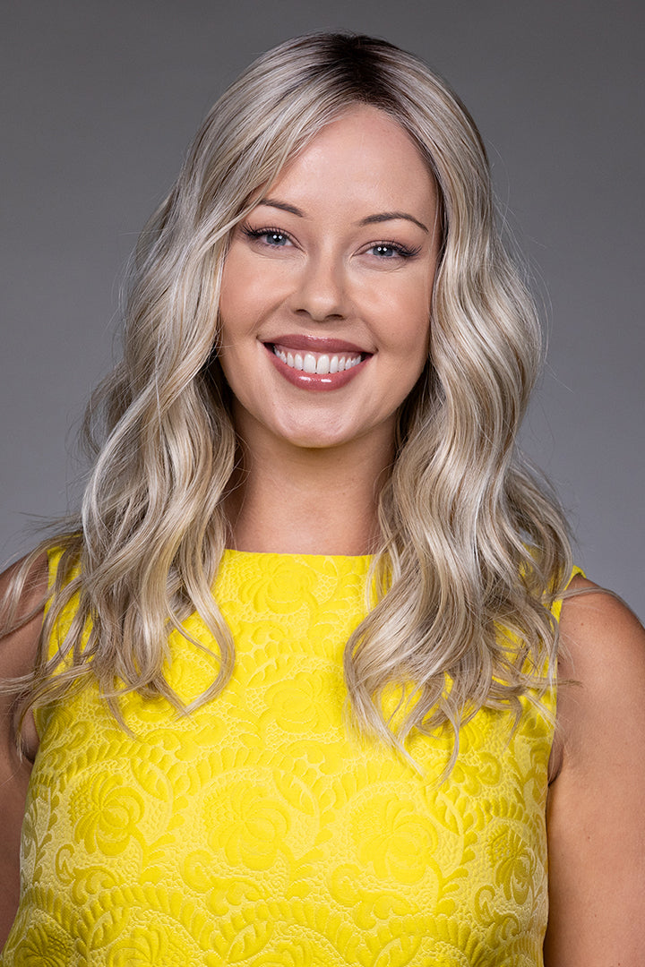 Bella by Belle Tress long blonde wavy synthetic wig with lace front and monofilament top on a smiling woman.