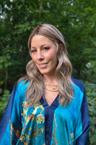 A woman with blonde-highlighted hair wearing a blue and teal floral kimono-style top (wearing Bella by Belle Tress in Brown Sugar Cookie R).