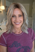 A smiling woman with shoulder-length wavy blonde wig (Monaco by Belle Tress in color Milkshake Blonde R).