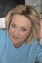 A  woman wearing chin length wispy blonde wig (Oslo by Belle Tress in color Milkshake Blonde R).