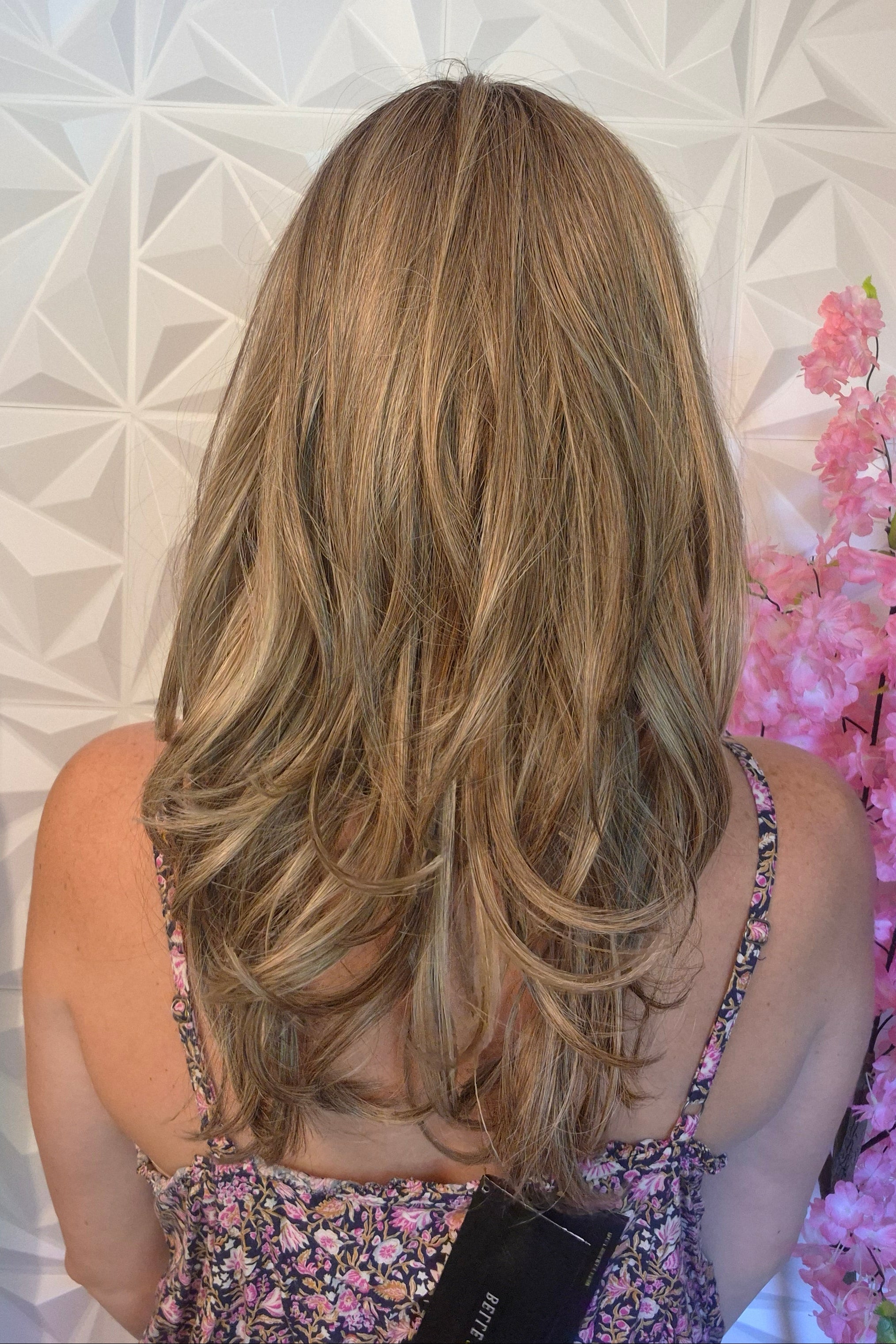 A woman with shoulder-length blonde hair and bangs wearing a floral-patterned camisole top (Marseille by Belle Tress in color Macadamia Latte R).
