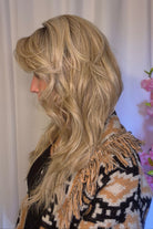 A woman with long blonde wavy wig withh bangs (Muse by Belle Tress in color Butterbeer R).