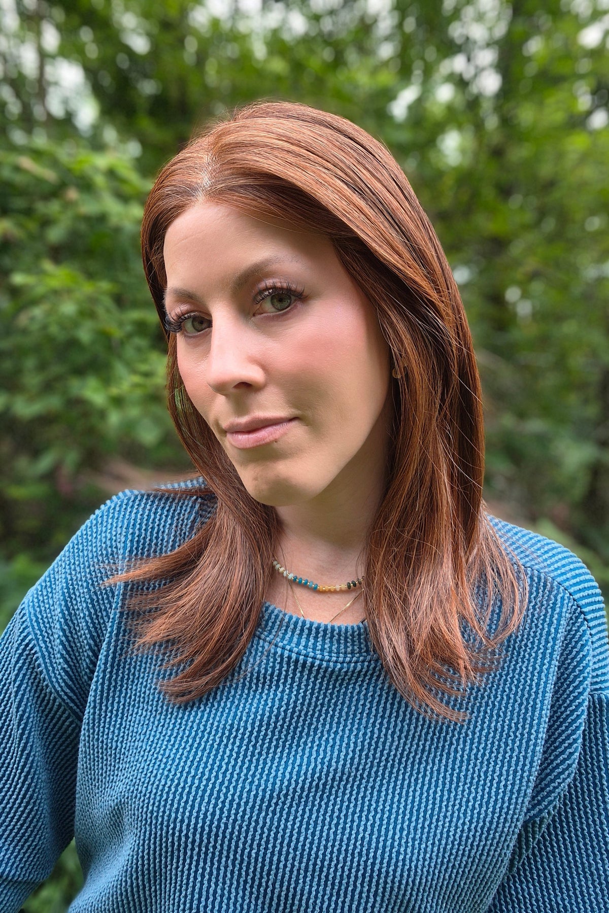 A woman with shoulder-length auburn hair wearing a blue ribbed knit sweater (Box Office Beauty by Raquel Welch in Cinnabar)