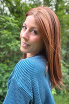 A woman with shoulder-length auburn hair wearing a blue ribbed knit sweater (Box Office Beauty by Raquel Welch in Cinnabar)