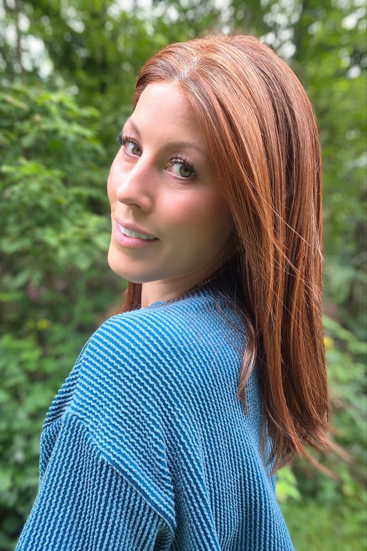 A woman with shoulder-length auburn hair wearing a blue ribbed knit sweater (Box Office Beauty by Raquel Welch in Cinnabar)