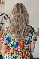 A woman with rooted blonde wavy hair wearing a vibrant, multicolored floral print top (Claudia by Belle Tress in Butterbeer R).