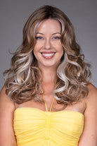 Dahlia by Belle Tress long wavy synthetic wig with wide center part and money piece highlights.